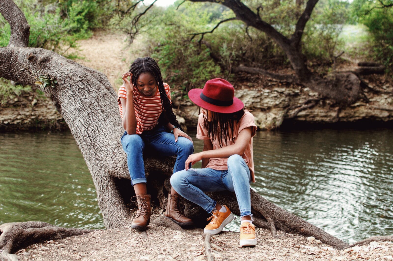 Two teenagers sitting on a log by a river, smiling and talking with one another.