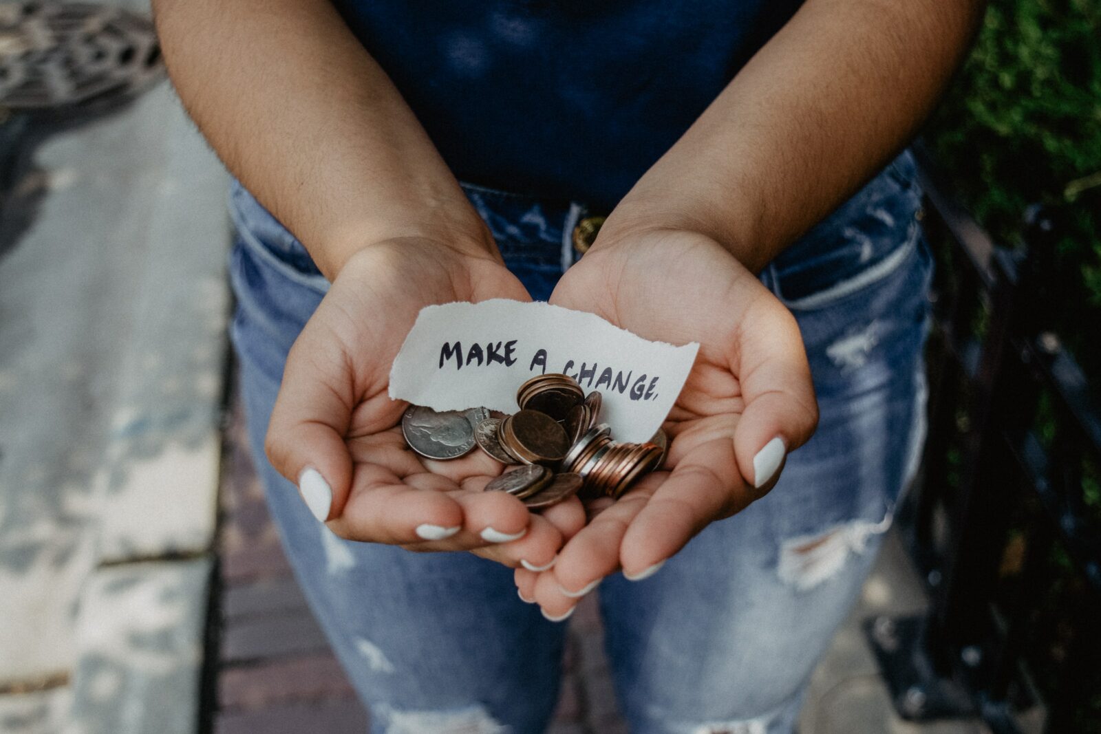 Person holding coins and a note in cupped hands. The note reads, "MAKE A CHANGE."